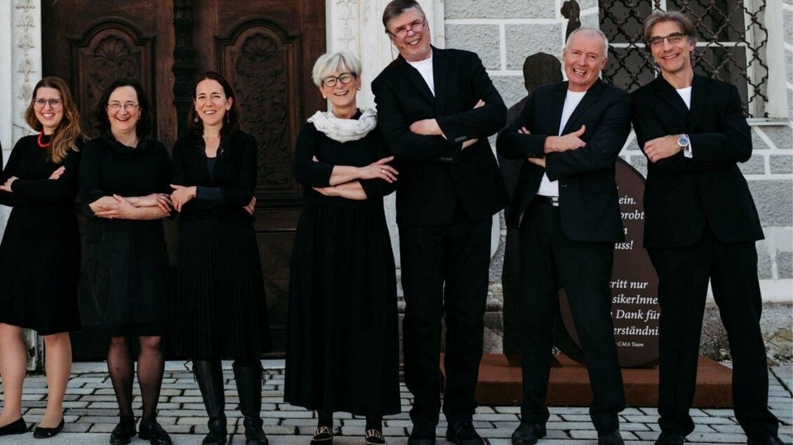 Eine Gruppe von sieben Personen steht nebeneinander und lächelt. Sie tragen schwarze Kleidung und haben eine freundliche Ausstrahlung. | © Ensemble Vokal