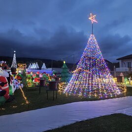 Ein festlich geschmückter Garten mit vielen bunten Lichtern und Weihnachtsfiguren. Im Mittelpunkt steht ein leuchtender Weihnachtsbaum und verschiedene Weihnachtsmänner. | © Wiesenhofer Stefan