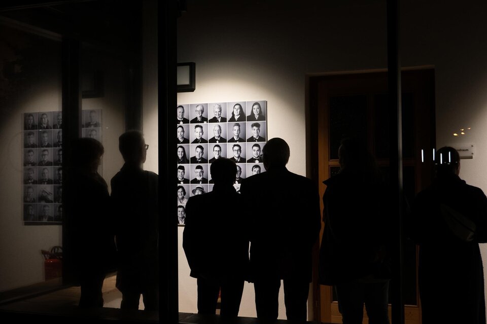 Eine Gruppe von Menschen steht vor einer Gallery. Im Hintergrund sind viele monochrome Porträts an der Wand zu sehen. | © Christian Koschar