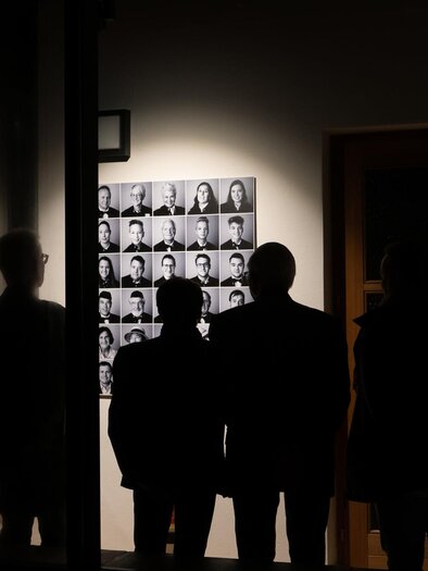 Eine Gruppe von Menschen steht vor einer Gallery. Im Hintergrund sind viele monochrome Porträts an der Wand zu sehen. | © Christian Koschar