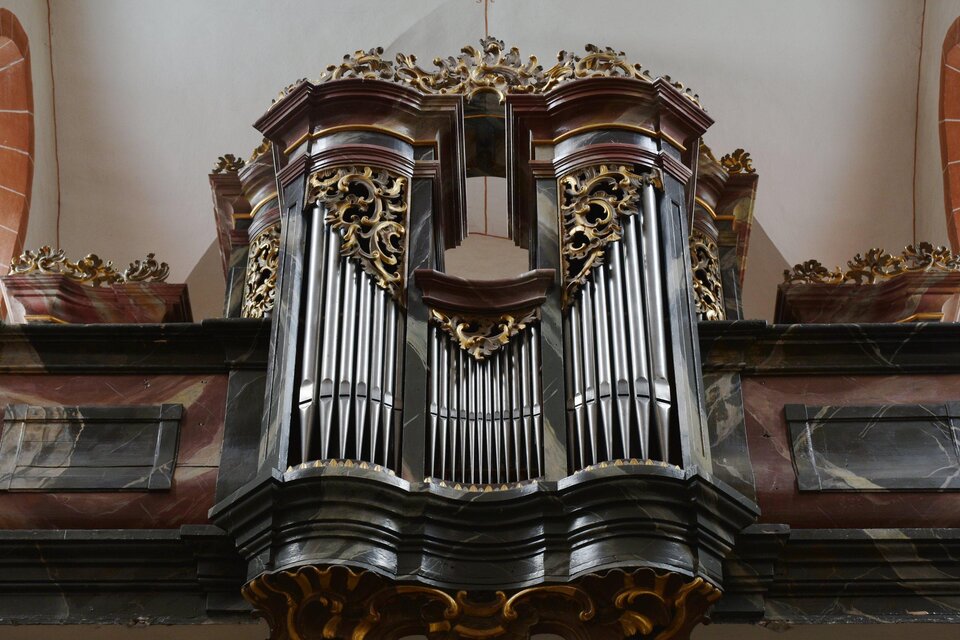 Eine beeindruckende Orgel mit kunstvollem Design und verzierten Details. Sie befindet sich in einem großen, lichtdurchfluteten Raum.