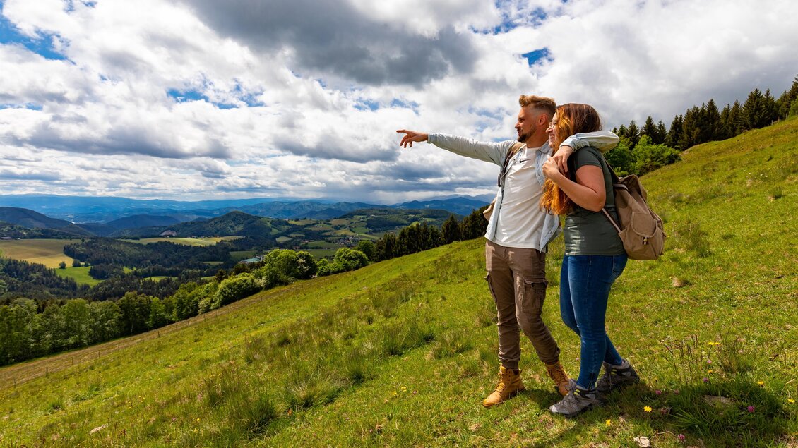 Wanderweg führt über eine Wiese, die Wanderer genießen die herrliche Aussicht. | © Region Graz-Harry Schiffer