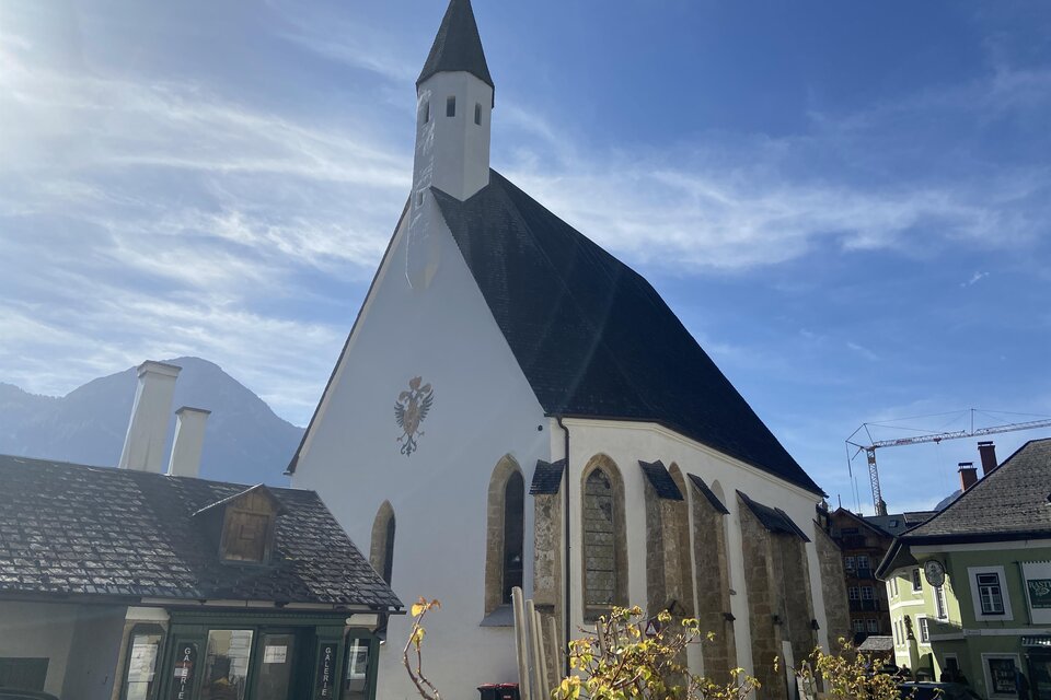Eine schöne Kirche mit einem spitzen Turm und einem klaren blauen Himmel. Die Fassadenfarbe ist überwiegend weiß mit einigen historischen Elementen. | © TVB Ausseerland Salzkammergut/Jana Grill