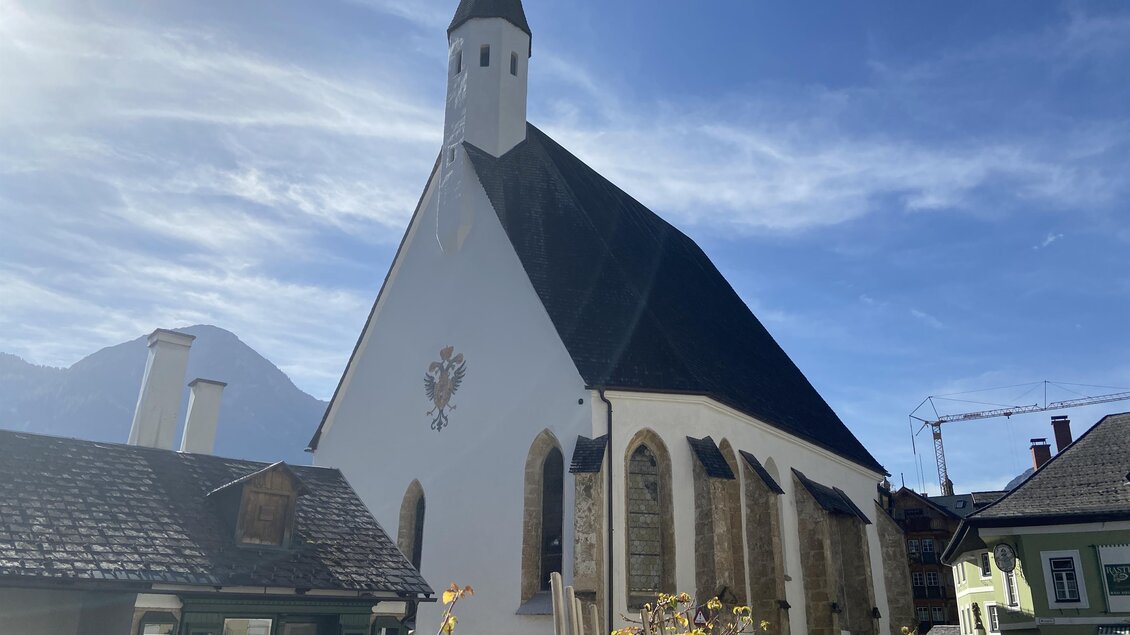 Eine schöne Kirche mit einem spitzen Turm und einem klaren blauen Himmel. Die Fassadenfarbe ist überwiegend weiß mit einigen historischen Elementen. | © TVB Ausseerland Salzkammergut/Jana Grill