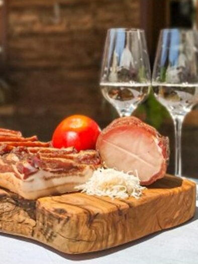 Eine rustikale Holzplatte mit verschiedenen Wurst- und Käseaufschnitten, einer Tomate und Sauerkraut. Dazu stehen zwei Gläser Wein und eine Flasche auf dem Tisch. | © Obsthof Wilhelm