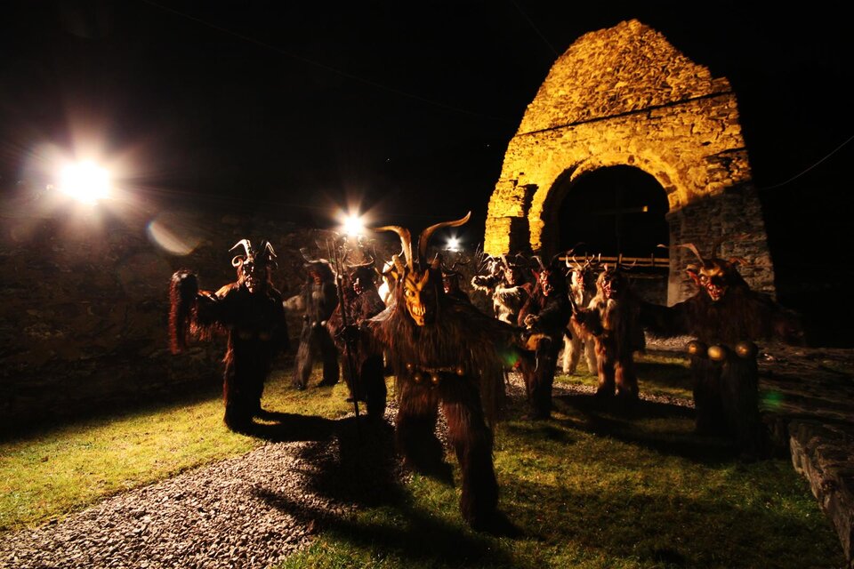 Eine Gruppe von Personen in traditionellen Kostümen steht in einem dunklen Bereich vor einer alten Ruine. Helle Scheinwerfer beleuchten die Szene und schaffen eine festliche Atmosphäre. | © Brauchtumsgruppe Erlsberg