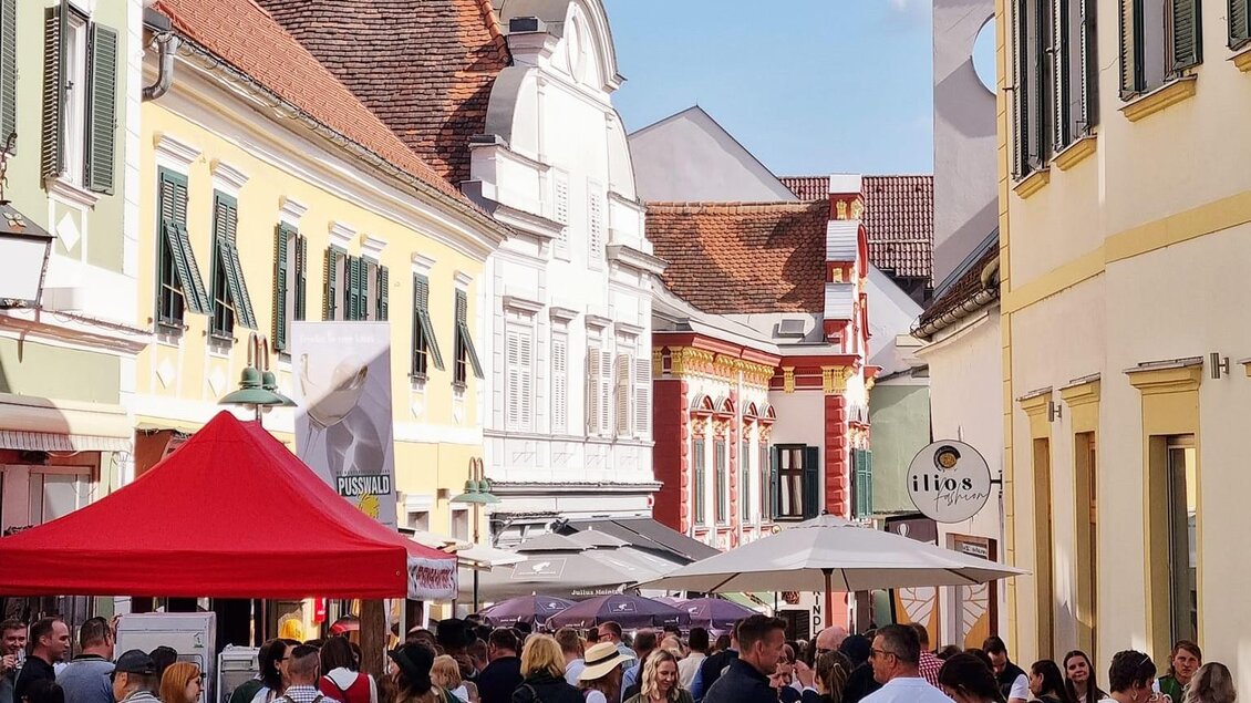 Eine belebte Straßenveranstaltung mit zahlreichen Menschen in traditioneller Kleidung. Bunte Marktstände und eine malerische Altstadt im Hintergrund. | © Stadtgemeinde Hartberg