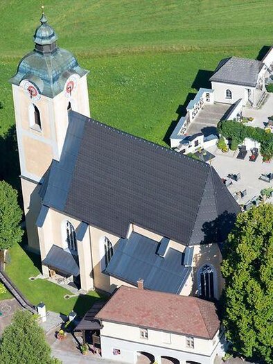 Eine historische Gebäudegruppe in einer ländlichen Umgebung, umgeben von Bäumen und Wiesen. Das Hauptgebäude hat einen charakteristischen Glockenturm. | © Diözese Graz Seckau