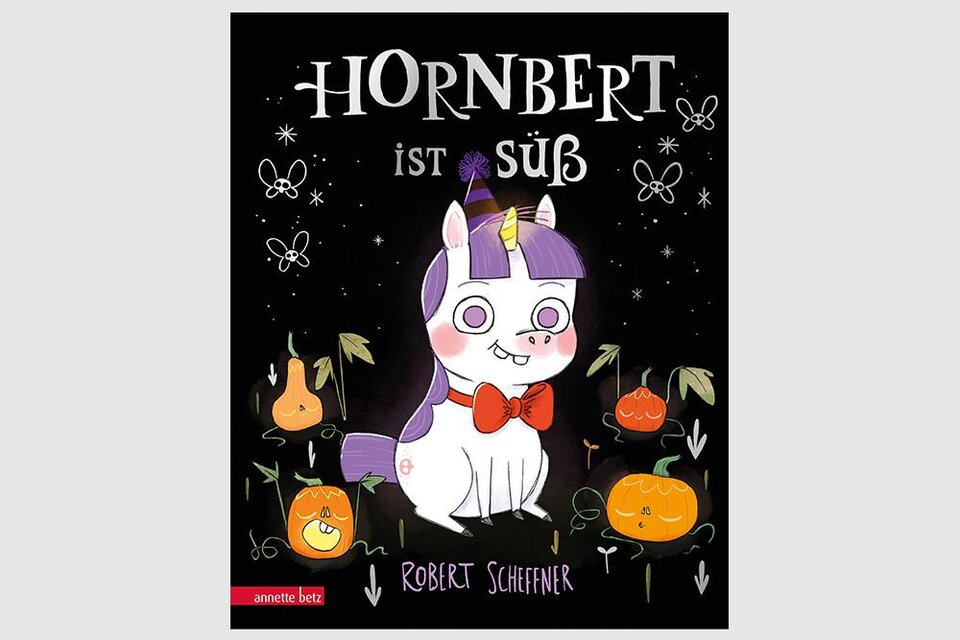 Ein niedliches Einhorn namens Hornbert mit einer roten Schleife. Im Hintergrund sind orangefarbene Früchte und fröhliche Motive zu sehen. | © Annette Betz