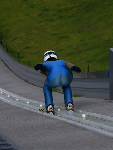 A ski jumper is preparing for the jump from a ski jumping facility. He is wearing a blue suit and shows a focused posture. | © Energie Steiermark Erzberg Arena