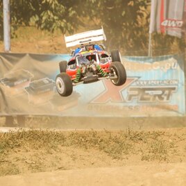Ein RC-Auto springt durch die Luft auf einer Rennstrecke. Im Hintergrund sind Werbebanner und Staubwolken zu sehen. | © Verein WMW-Buggy Racing