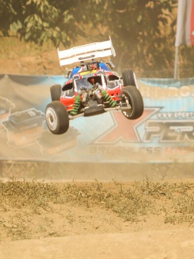 Ein RC-Auto springt durch die Luft auf einer Rennstrecke. Im Hintergrund sind Werbebanner und Staubwolken zu sehen. | © Verein WMW-Buggy Racing