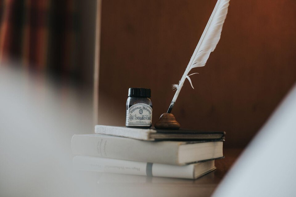 Ein Federkiel und ein Tintenfass stehen auf einem Stapel Bücher. Im Hintergrund sind sanfte Farben und eine warme Atmosphäre zu sehen. | © Die Wasnerin