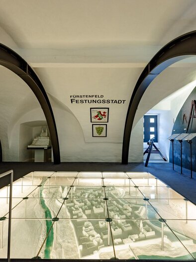 Ein Ausstellungsraum mit modernen Bögen und einem Diorama einer Festungsstadt. Die Wände sind mit Informationen und Erklärungen zur Geschichte der Stadt dekoriert. | © Stadtmarketing Fürstenfeld