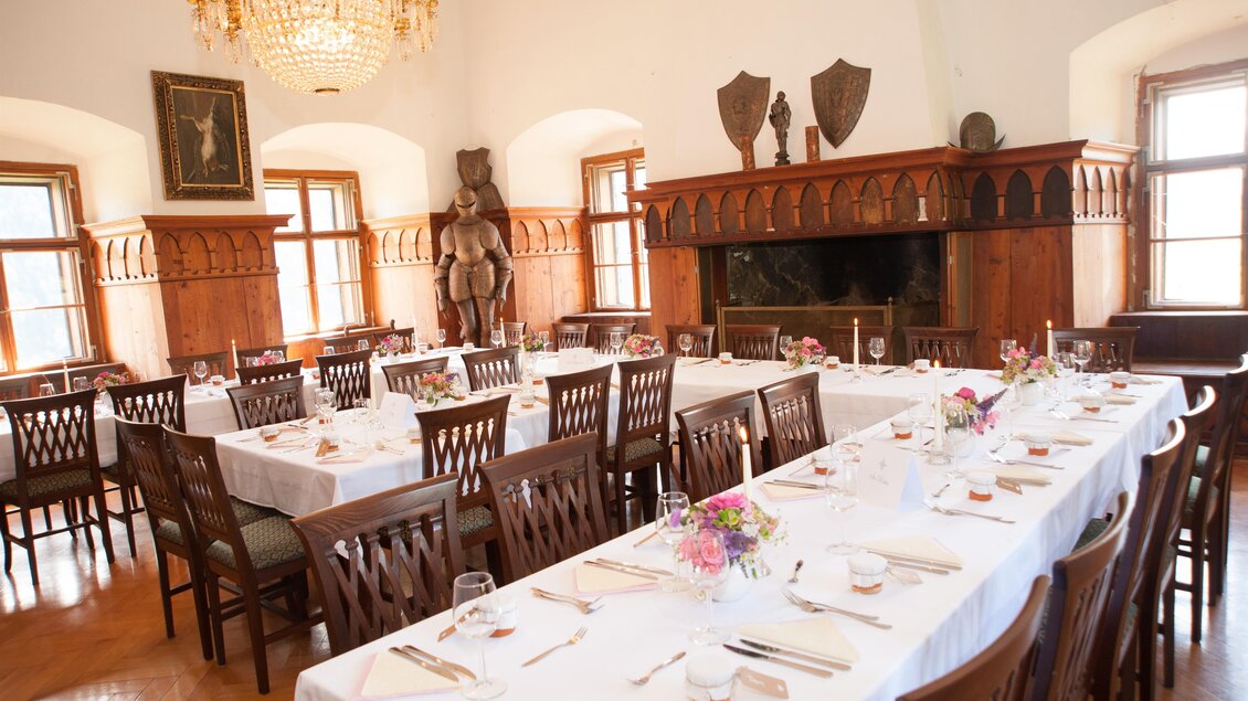 Ein eleganter Speisesaal mit einem langen Tisch, der mit Blumen und Geschirr gedeckt ist. Die Wände sind mit Holzverkleidungen und dekorativen Elementen geschmückt. | © Fam. Steiner