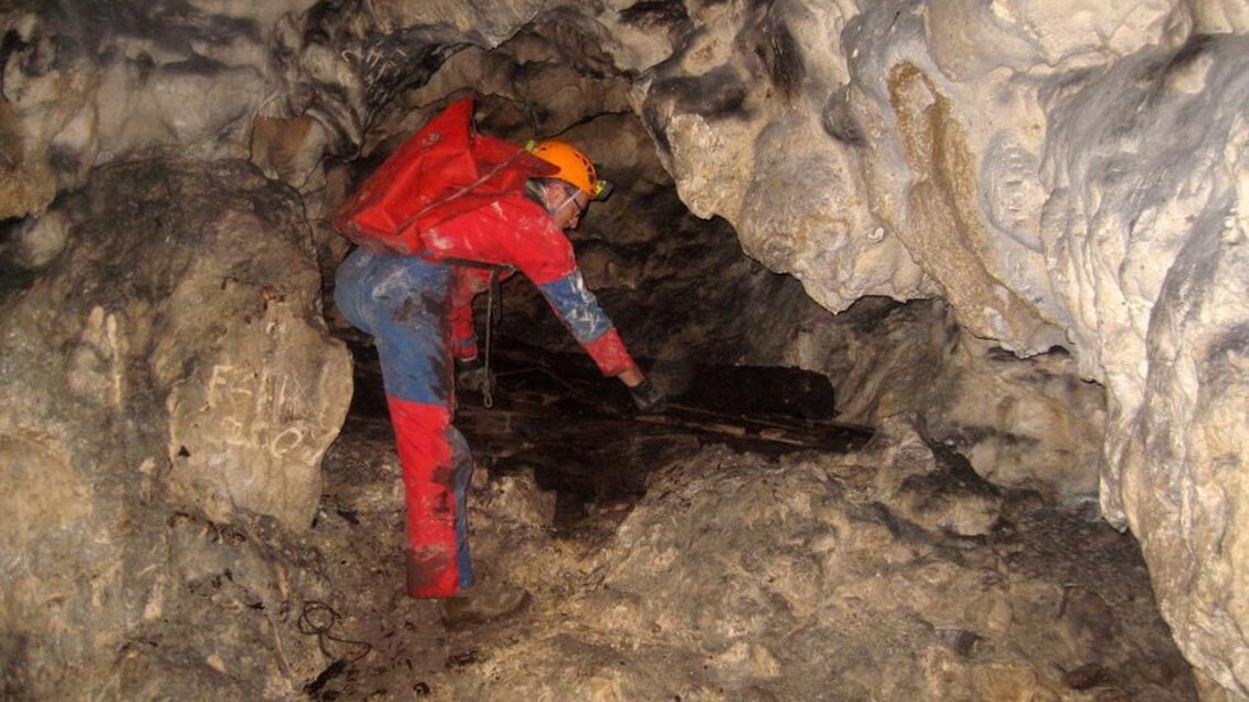 Ein Höhlenforscher in Schutzausrüstung untersucht eine dunkle Höhle. Die Wände sind rau und die Umgebung scheint feucht zu sein. | © www.hohlensteinhoehle.at