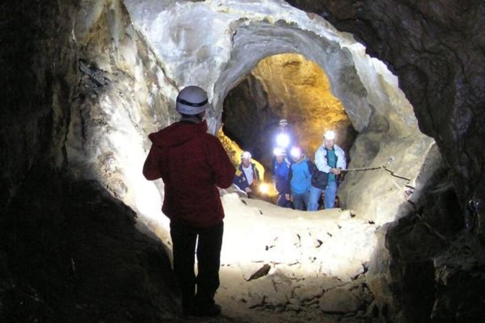 Eine Gruppe von Menschen mit Helmen wandert durch eine Höhle. Das Licht ihrer Lampen erhellt den engen Tunnel.