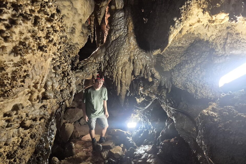 Eine Person steht in einer Höhle mit Stalaktiten und Stalagmiten. Die Szenerie ist schwach beleuchtet, mit einigen Lichtquellen, die den Weg erhellen. | © Andrea Stelzer