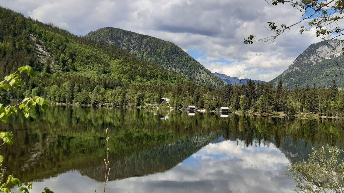 Im klaren Wasser des Ödensees spiegeln sich die beeindruckende Bergkulisse des Ausseerlandes und zwei idyllische Bootshütten. | © Daniela Casari