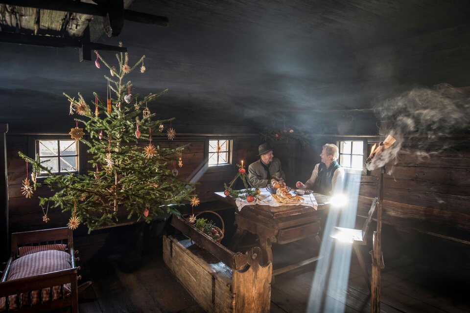 Ein gemütlicher, rustikaler Raum mit einem schön geschmückten Weihnachtsbaum. Zwei Personen sitzen an einem Tisch und genießen eine festliche Mahlzeit. | © ÖFM-Johannes Kernmayer