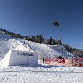Ein Skifahrer springt über einen Sprung im Schnee. Im Hintergrund sind Bäume und ein blauer Himmel zu sehen. | © TVB Murau