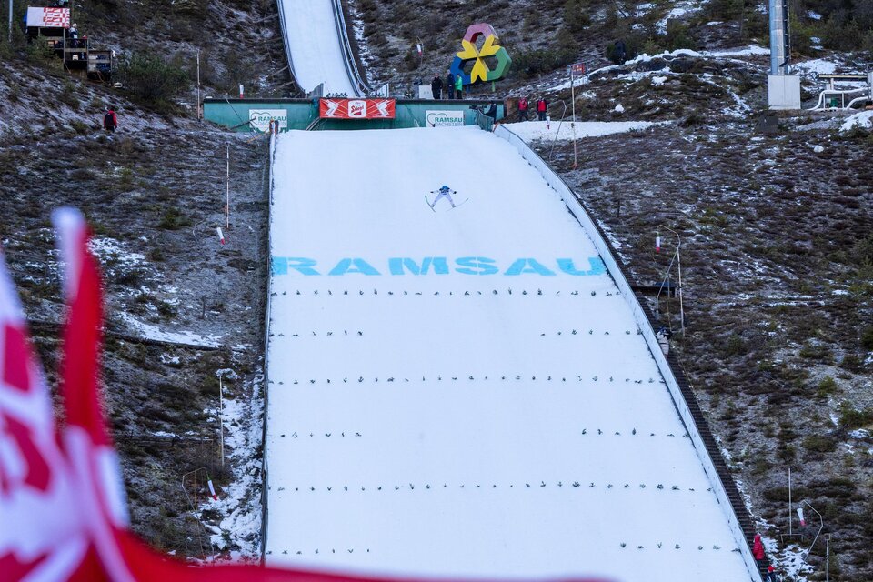 Eine Skisprungschanze in Ramsau mit verschneiter Landebahn. Im Vordergrund wehen die roten Flaggen im Wind.