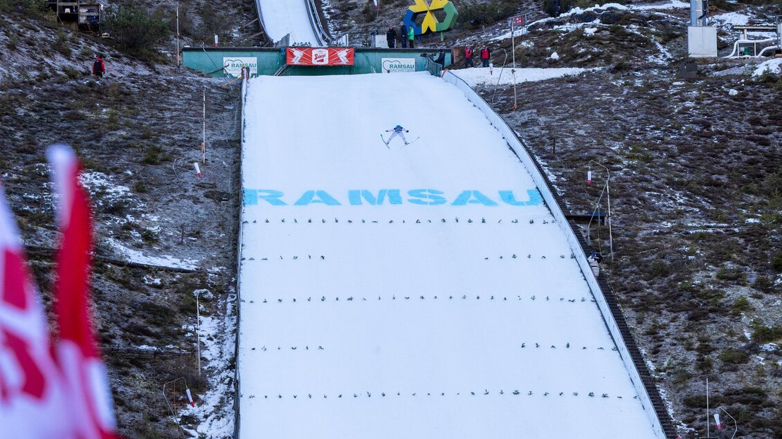 Eine Skisprungschanze in Ramsau mit verschneiter Landebahn. Im Vordergrund wehen die roten Flaggen im Wind.