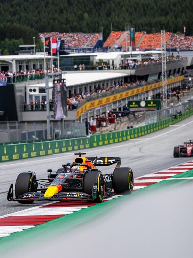 A Formula 1 racing car is driving on the racetrack, surrounded by a lively crowd of spectators. In the background, the pit lane and the mountains can be seen. | © Joerg Mitter Red Bull Ring