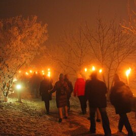 A group of people with torches walks through a wintry landscape. Trees are covered with frost and the scene has a mystical atmosphere.