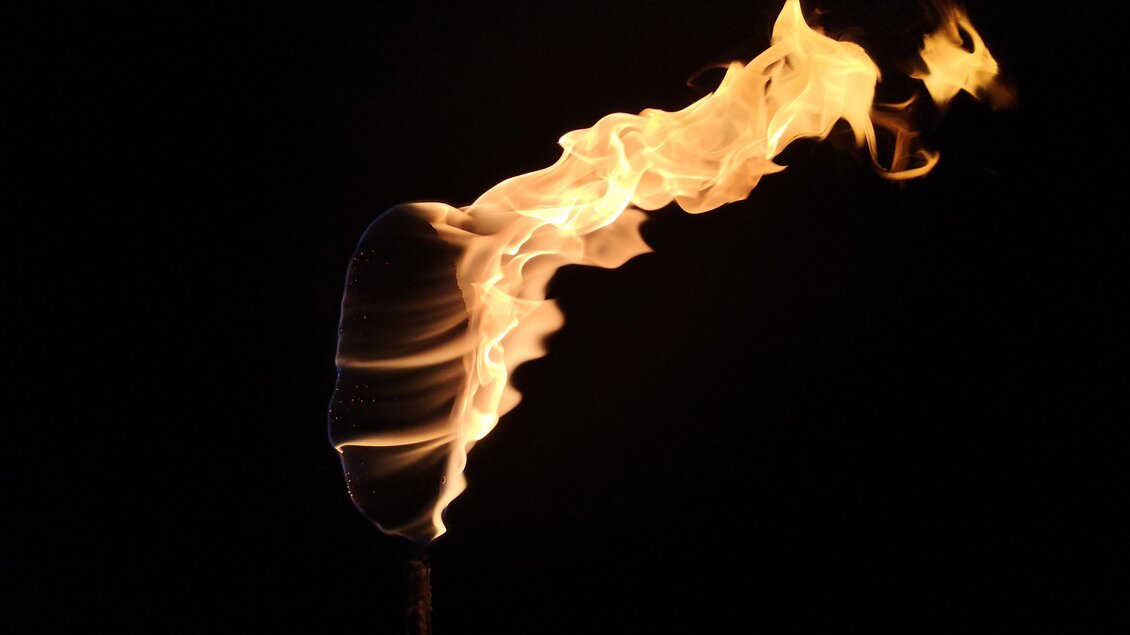 Nahaufnahme einer brennenden Fackel mit orangegelben Flammen vor schwarzem Nachthimmel. | © Surwhyve