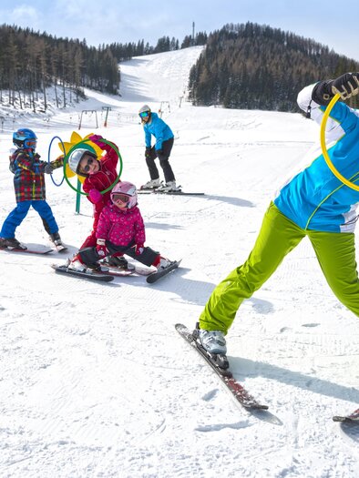 Eine Gruppe von Kindern und einem Erwachsenen fährt Ski im Schnee. Die Kinder haben Spaß mit Reifen auf der Piste. | © Tourismusverband Oststeiermark