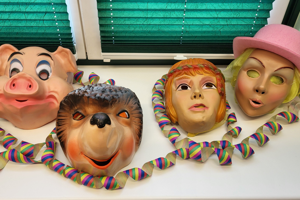 Bunte Masken von einem Schwein, einem Igel und zwei Menschen, die an einem Tisch angeordnet sind. Neben den Masken liegen farbige Papierschlangen. | © Petra Kirchschlager
