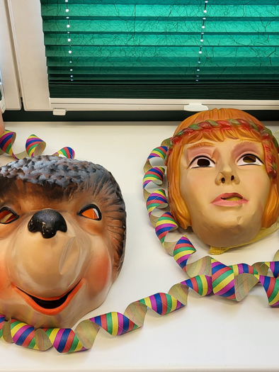 Colorful masks of a pig, a hedgehog, and two people arranged on a table. Next to the masks are colorful paper streamers. | © Petra Kirchschlager