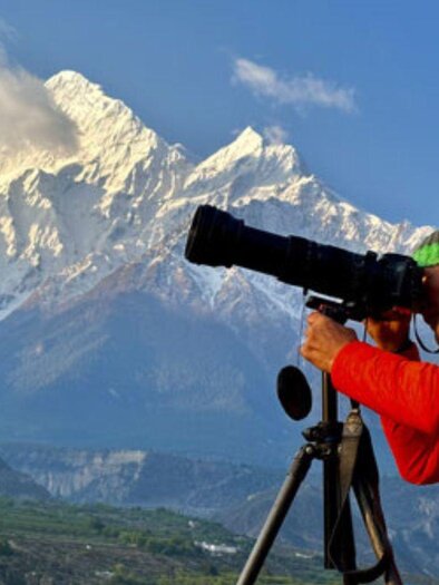 <p>Helmut Pichler steht inmitten der atemberaubenden Himalaya Landschaft mit seiner Kamera und einem Stativ und fotografiert die Natur.</p> | © Helmut Pichler