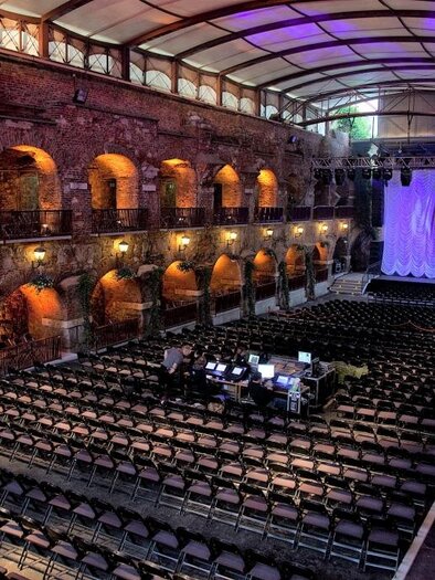 Eine große Innenhalle mit vielen leeren Stühlen. Im Hintergrund befindet sich eine Bühne mit dekorativer Beleuchtung. | © c_Palme-Pete