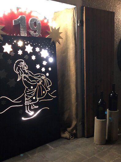 Atmospherically illuminated Advent window at the wine estate Gwaltl, featuring star motifs and a Christmas depiction. | © Weinhof Gwaltl
