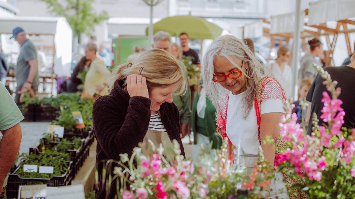 Ein lebendiger Marktplatz mit vielen Pflanzen und Blumen. Zwei Frauen betrachten interessiert die angebotenen Pflanzen. | © Anna Zora