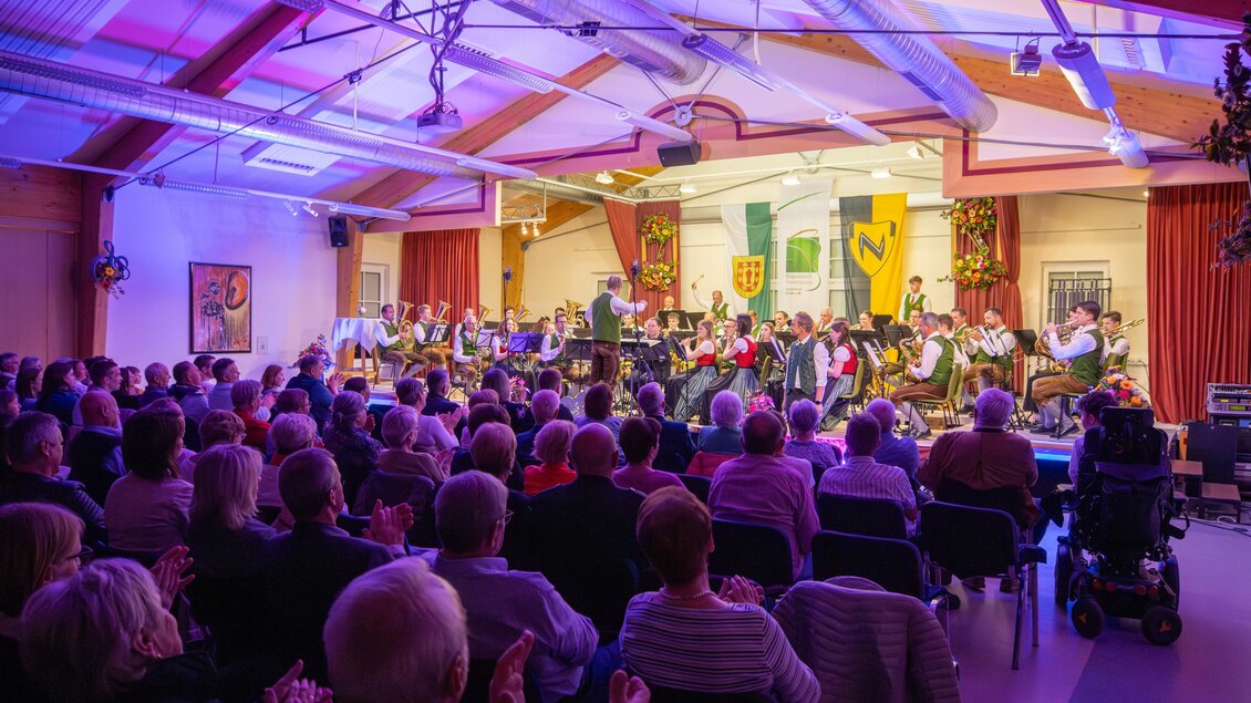 Ein großes Konzert mit einem Orchester auf der Bühne. Viele Zuschauer sitzen und applaudieren in einem festlichen Raum. | © Mittlinger