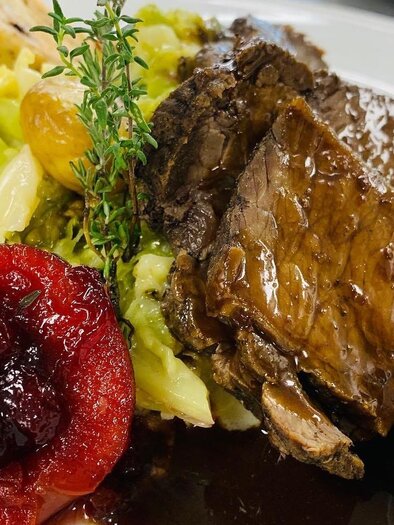 Ein köstlicher Teller mit zartem Fleisch, Beilagen aus Gemüse und Klößen. Das Gericht wird mit Preiselbeeren und einer Kräuterdekoration serviert. | © Wirtshaus Meißl