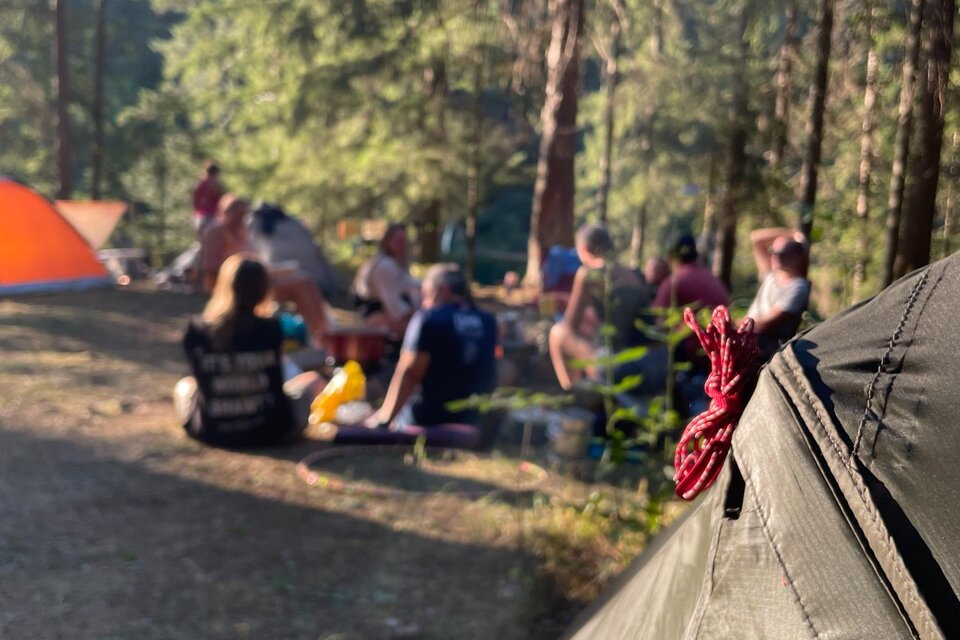 Gruppe auf einem Zeltlagerplatz im Wald am Hirzmann-Stausee, mit mehreren Zelten im Hintergrund. | © Julia C. Pirkenau
