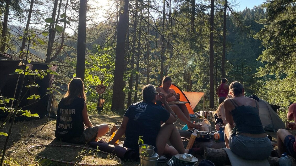 Erwachsene sitzen zwischen Zelten auf einem Zeltlagerplatz im Wald am Hirzmann-Stausee. | © Julia C. Pirkenau