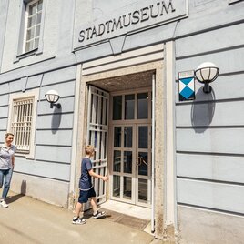 Eine Familie verlässt das Stadtmuseum. Das Gebäude hat eine helle Fassade mit einem klaren Eingang und modernen Lampen. | © WolfgangSpekner
