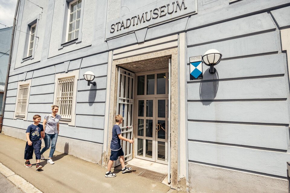Eine Familie verlässt das Stadtmuseum. Das Gebäude hat eine helle Fassade mit einem klaren Eingang und modernen Lampen. | © WolfgangSpekner