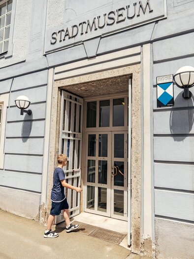 Eine Familie verlässt das Stadtmuseum. Das Gebäude hat eine helle Fassade mit einem klaren Eingang und modernen Lampen. | © WolfgangSpekner