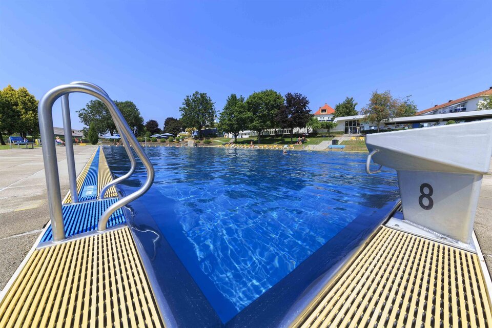 Ein Schwimmbecken mit klarem, blauem Wasser und einer Treppe. Im Hintergrund sind Bäume und Gebäude zu sehen, die eine entspannte Atmosphäre schaffen. | © Chris Zenz