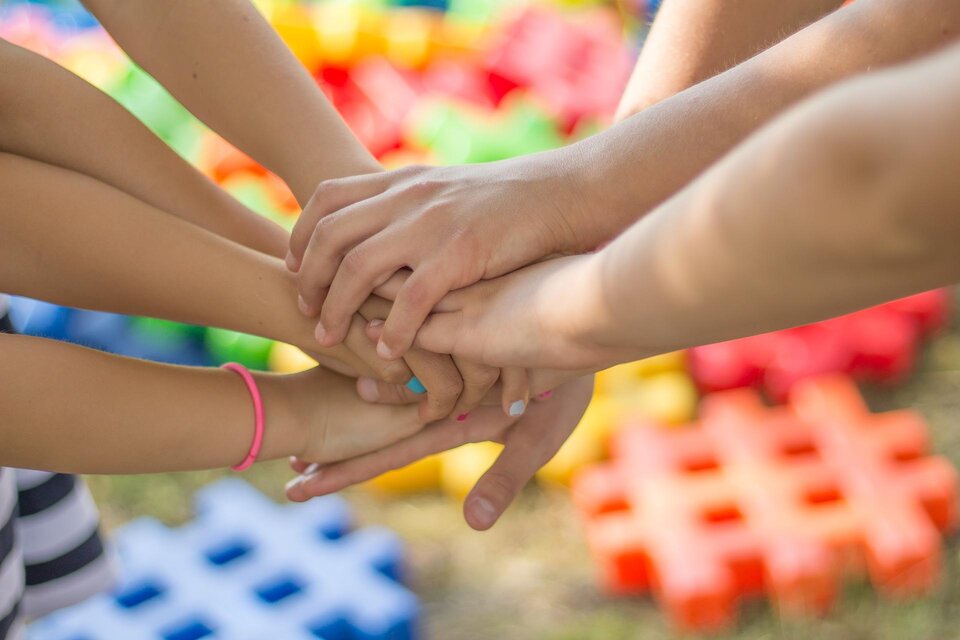 Viele Hände, die übereinanderliegen, symbolisieren Teamarbeit und Zusammenhalt. Im Hintergrund sind bunte Spielmatten sichtbar. | © Pixabay