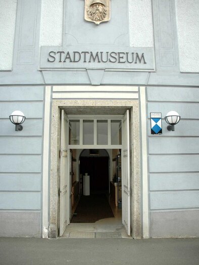 Entrance to the city museum with a clear sign above the door. The facade is light gray and has classic lamps on the sides. | © Stadtgemeinde Judenburg