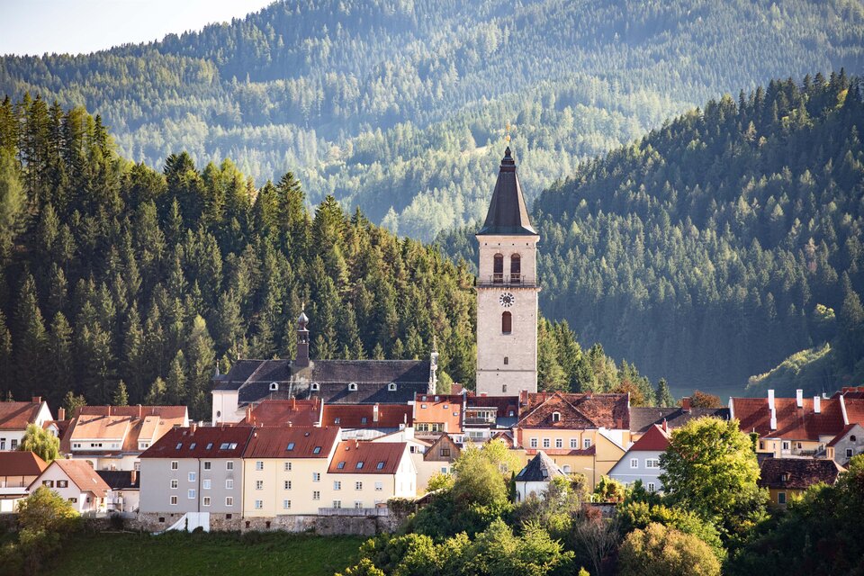Eine malerische Stadt mit einer markanten Kirche und roten Dächern. Umgeben von grünen Bergen und Wäldern. | © Anita Fössl