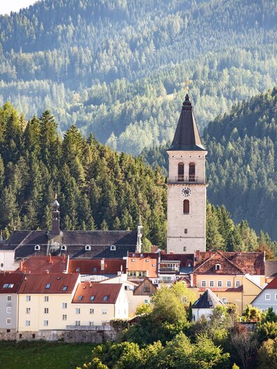 Eine malerische Stadt mit einer markanten Kirche und roten Dächern. Umgeben von grünen Bergen und Wäldern. | © Anita Fössl
