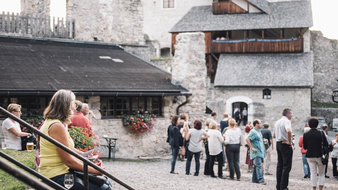 Eine gesellige Veranstaltung im Freien vor einer alten Burg. Menschen stehen, unterhalten sich und genießen die Atmosphäre.